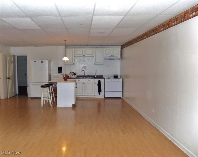 kitchen with a breakfast bar, pendant lighting, white cabinets, white appliances, and light wood-type flooring