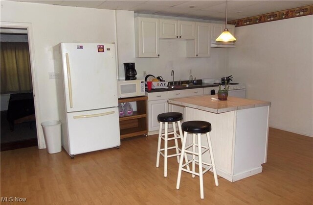 kitchen with a breakfast bar, white cabinets, hanging light fixtures, white appliances, and light hardwood / wood-style flooring