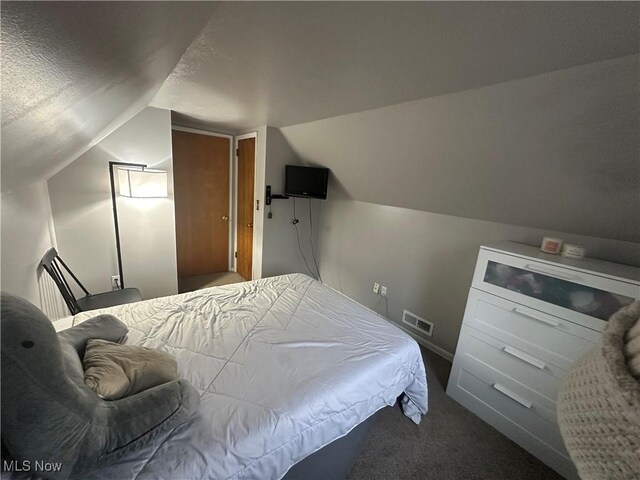 bedroom with lofted ceiling, a textured ceiling, and dark colored carpet