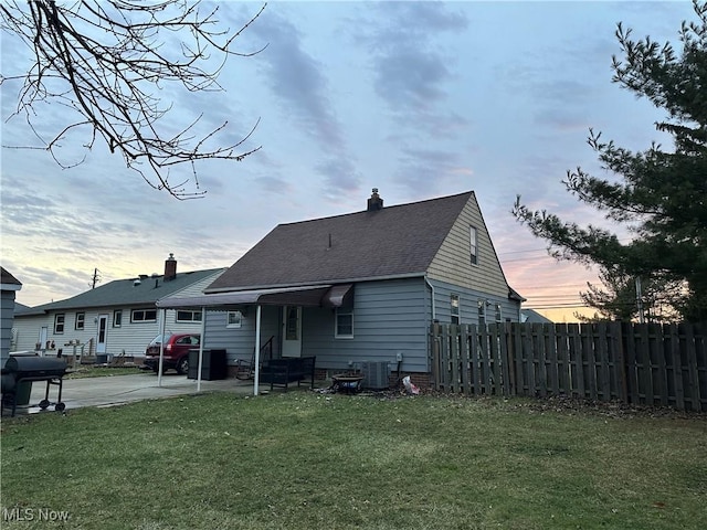 back house at dusk featuring cooling unit, a yard, and a patio area