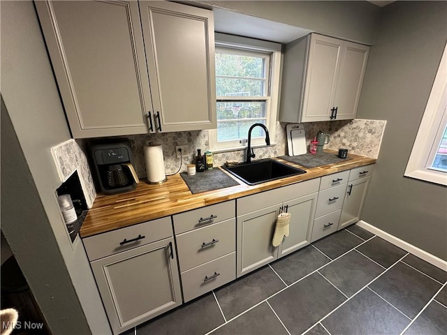 kitchen with dark tile patterned floors, sink, backsplash, and wood counters