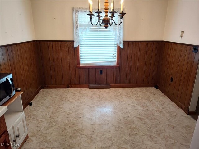 unfurnished dining area featuring a chandelier and wood walls