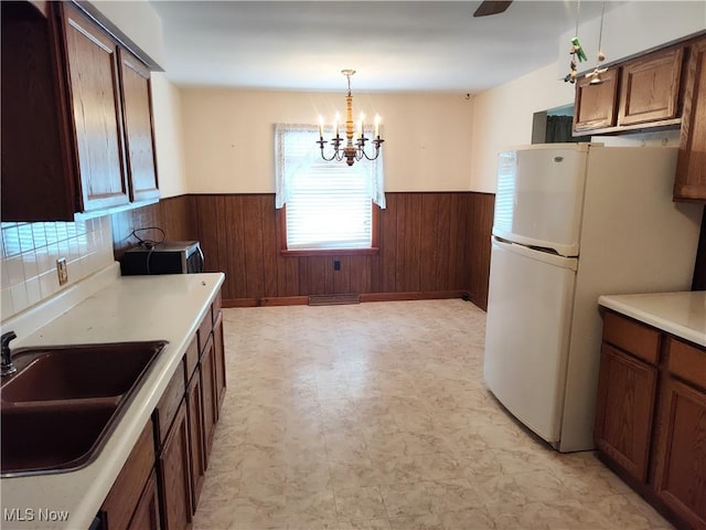 kitchen with white fridge, sink, pendant lighting, and wooden walls