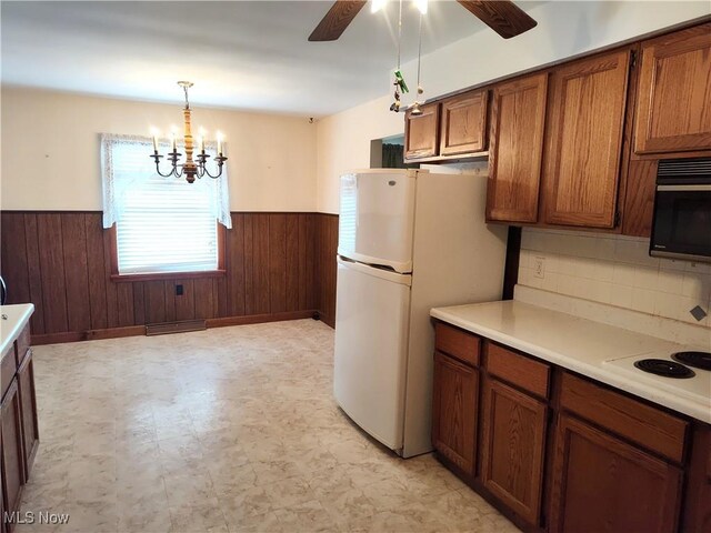 kitchen with wood walls, pendant lighting, white appliances, ceiling fan with notable chandelier, and decorative backsplash