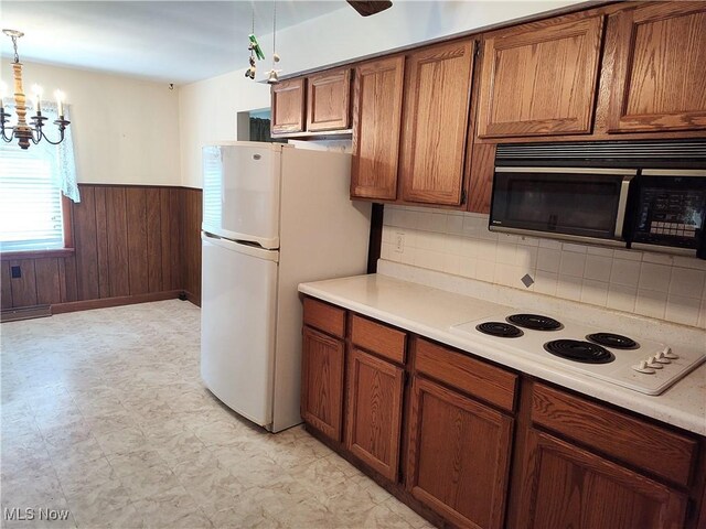 kitchen with a chandelier, wooden walls, pendant lighting, white appliances, and backsplash