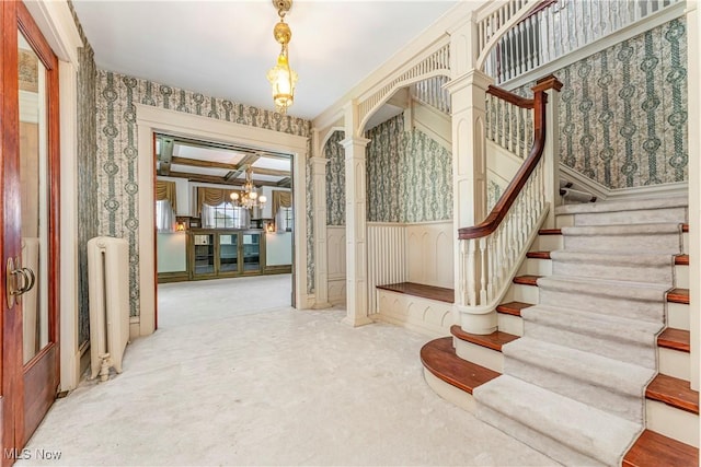 interior space featuring ornate columns, radiator heating unit, carpet floors, a notable chandelier, and beamed ceiling