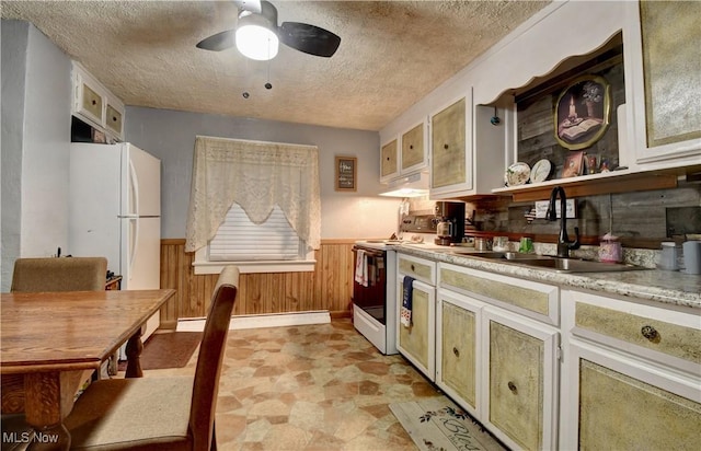 kitchen featuring sink, white appliances, a baseboard heating unit, wooden walls, and a textured ceiling