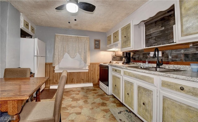 kitchen featuring sink, a textured ceiling, wooden walls, white appliances, and a baseboard heating unit