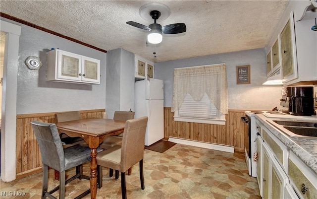 dining space with ceiling fan, a baseboard radiator, wooden walls, and a textured ceiling