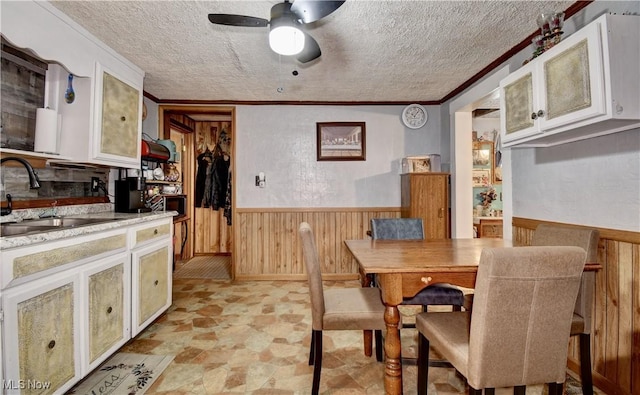 dining space with ornamental molding, sink, wooden walls, and a textured ceiling