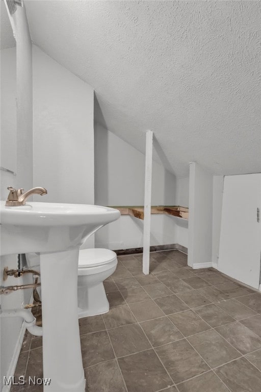 bathroom featuring lofted ceiling, toilet, tile patterned flooring, and a textured ceiling