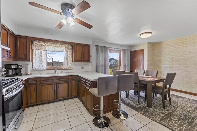 kitchen with light tile patterned flooring, brick wall, stainless steel range with gas cooktop, sink, and kitchen peninsula