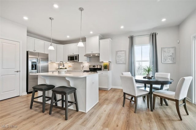 kitchen with white cabinetry, appliances with stainless steel finishes, hanging light fixtures, and a center island with sink