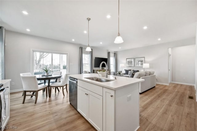 kitchen featuring sink, white cabinetry, hanging light fixtures, stainless steel dishwasher, and an island with sink