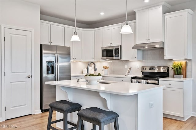 kitchen featuring hanging light fixtures, stainless steel appliances, an island with sink, white cabinets, and decorative backsplash