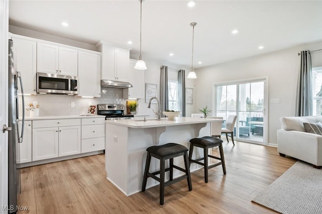 kitchen with appliances with stainless steel finishes, white cabinetry, backsplash, a center island with sink, and decorative light fixtures