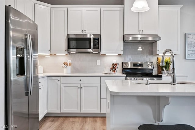 kitchen featuring white cabinetry, stainless steel appliances, decorative backsplash, decorative light fixtures, and light wood-type flooring