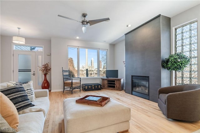 living room with ceiling fan, a large fireplace, plenty of natural light, and light wood-type flooring