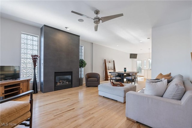 living room featuring a tiled fireplace, ceiling fan, and light wood-type flooring