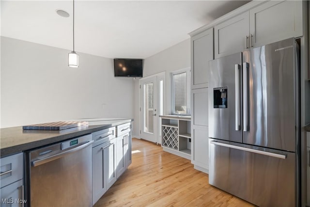 kitchen featuring appliances with stainless steel finishes, decorative light fixtures, gray cabinetry, dark stone countertops, and light hardwood / wood-style floors