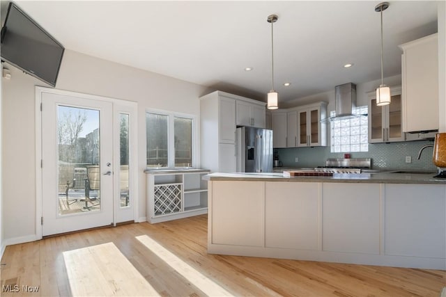 kitchen featuring sink, hanging light fixtures, kitchen peninsula, high end fridge, and wall chimney range hood