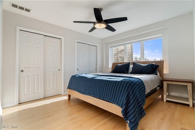 bedroom featuring two closets, ceiling fan, and light hardwood / wood-style flooring