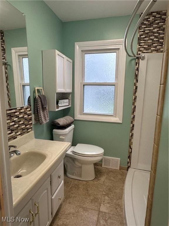 bathroom with vanity, a shower, a wealth of natural light, and backsplash