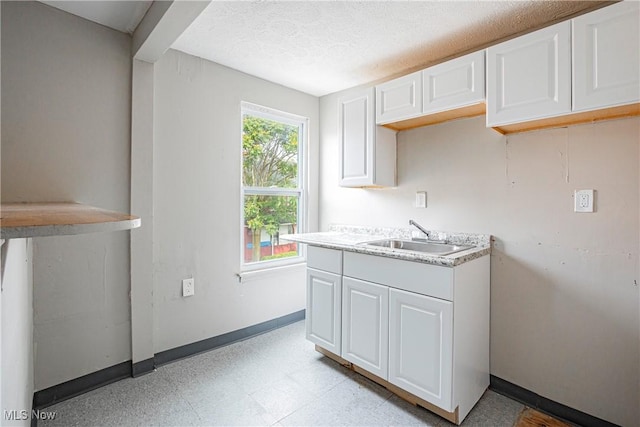 kitchen with sink, a textured ceiling, and white cabinets