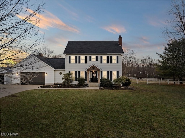 colonial inspired home with a garage and a lawn