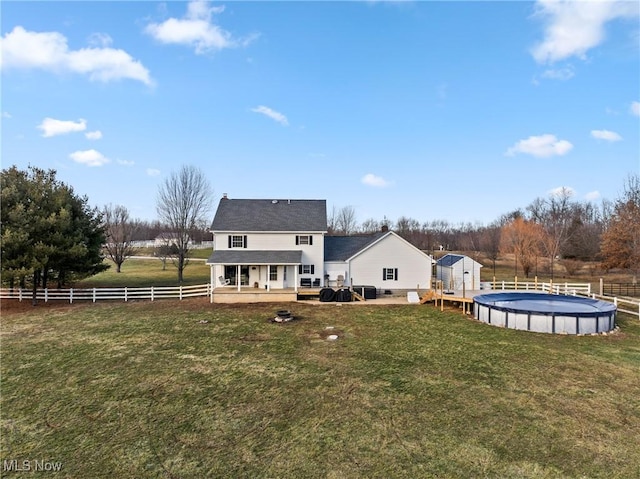 rear view of house featuring a fenced in pool, a lawn, and a rural view