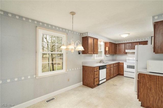 kitchen featuring pendant lighting, white appliances, sink, and a notable chandelier