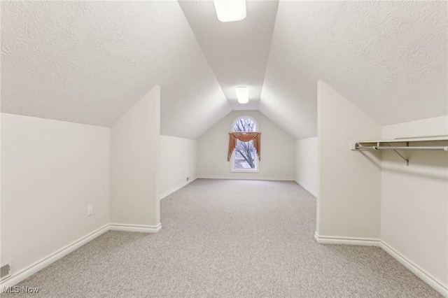 additional living space featuring vaulted ceiling, light carpet, and a textured ceiling