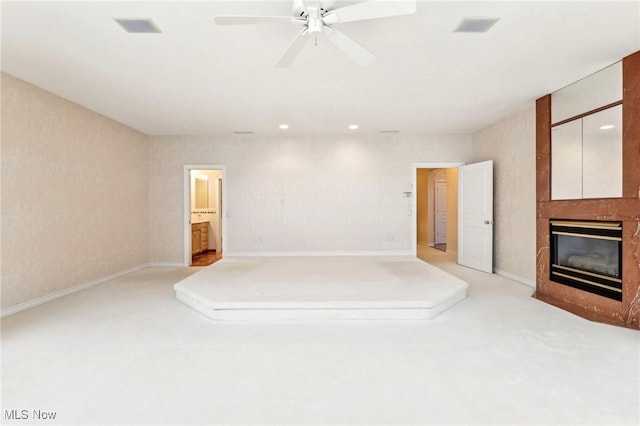 interior space with ceiling fan, a large fireplace, light carpet, and ensuite bath