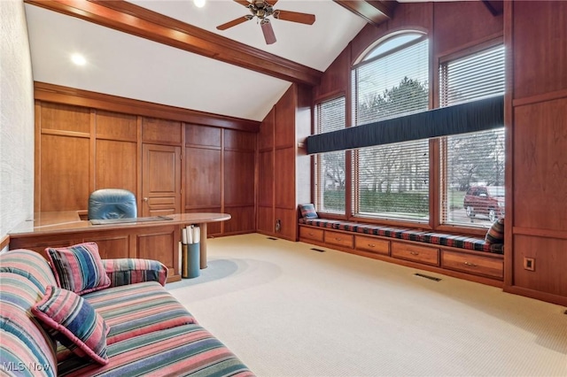 carpeted office space featuring vaulted ceiling with beams, ceiling fan, and wood walls