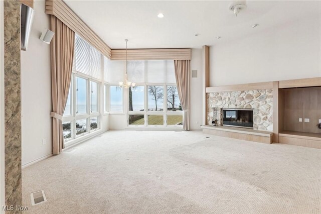 unfurnished living room with a stone fireplace, a chandelier, and carpet floors