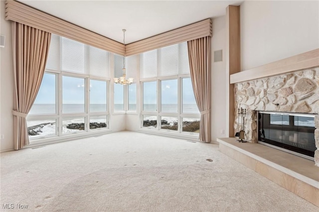 unfurnished living room with a towering ceiling, a fireplace, carpet floors, a water view, and an inviting chandelier