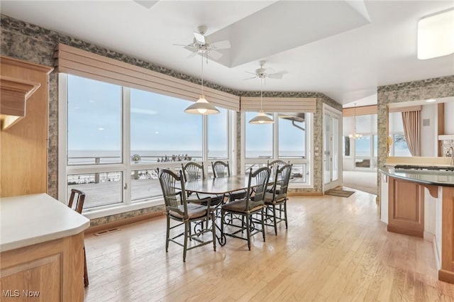 dining space featuring ceiling fan, a water view, and light wood-type flooring