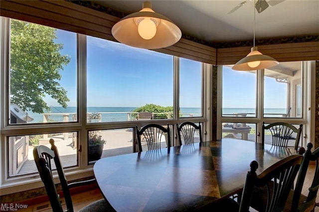 dining area with hardwood / wood-style flooring, expansive windows, ceiling fan, and a water view