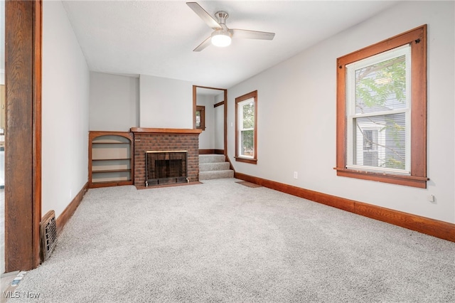 unfurnished living room featuring ceiling fan, a brick fireplace, a healthy amount of sunlight, and carpet flooring