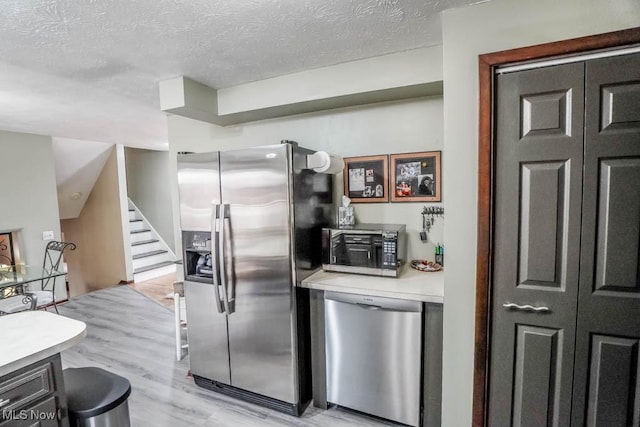 kitchen with stainless steel appliances, a textured ceiling, and light wood-type flooring