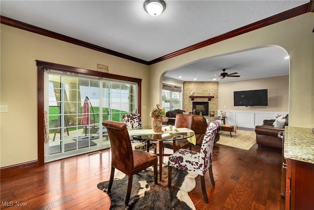 dining area with ornamental molding, dark wood-type flooring, a large fireplace, and ceiling fan