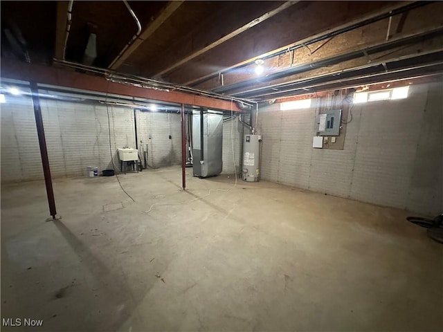 below grade area with electric panel, water heater, a sink, brick wall, and heating unit