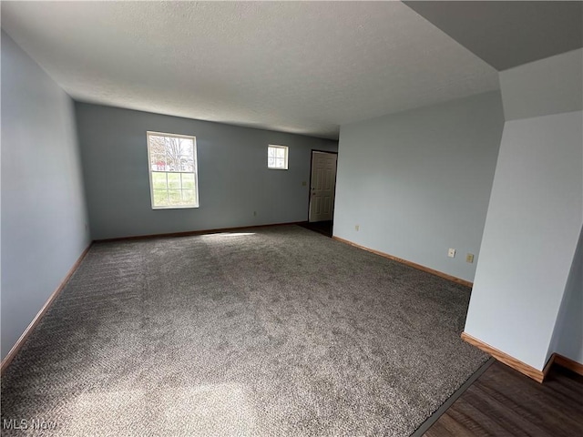 empty room with a textured ceiling, baseboards, and carpet
