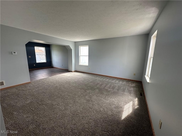 carpeted empty room with arched walkways, visible vents, a textured ceiling, and baseboards