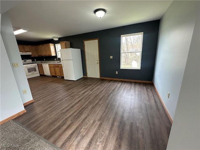 kitchen with dark wood finished floors, under cabinet range hood, a sink, and white appliances