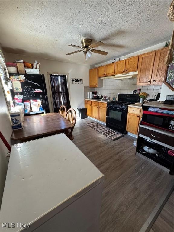 kitchen with dark wood-type flooring, decorative backsplash, ceiling fan, and black gas range