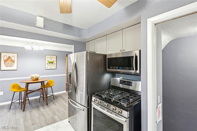 kitchen featuring pendant lighting, appliances with stainless steel finishes, white cabinetry, light hardwood / wood-style floors, and ceiling fan with notable chandelier