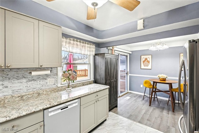 kitchen with light stone counters, hanging light fixtures, stainless steel appliances, ceiling fan with notable chandelier, and backsplash