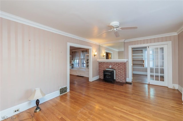 unfurnished living room with a wood stove, ornamental molding, a wealth of natural light, ceiling fan, and light hardwood / wood-style floors