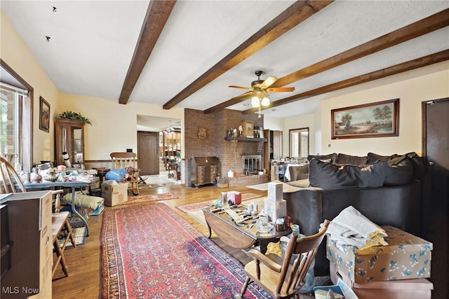 living room featuring hardwood / wood-style floors, beam ceiling, a fireplace, and ceiling fan